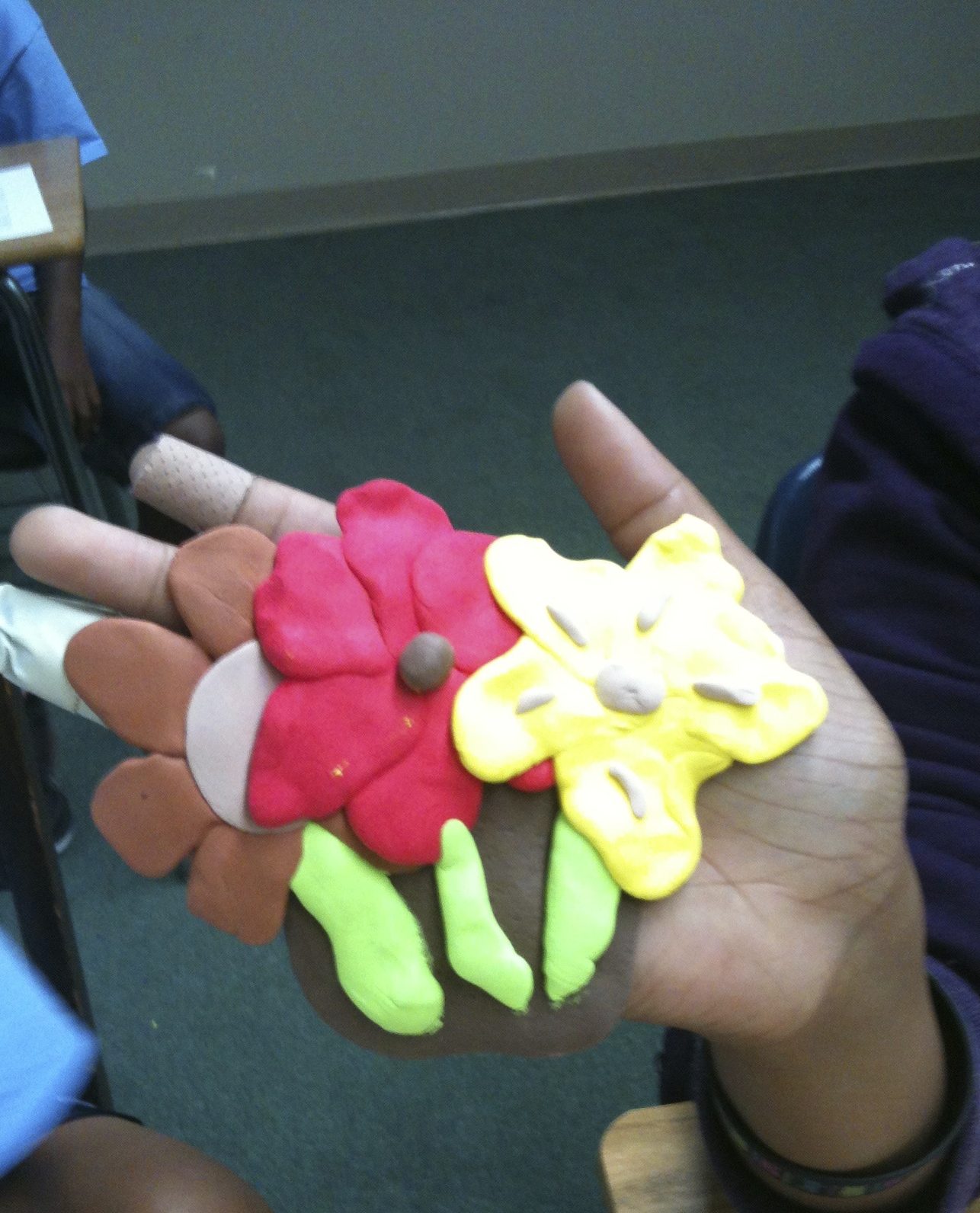 Sculpture in a child's hand of three flowers with different colors.